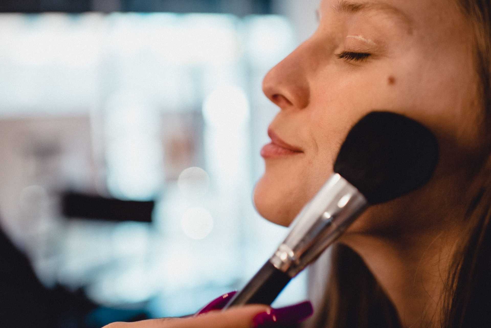 Woman having her makeup applied with a brush, eyes closed and relaxed expression.