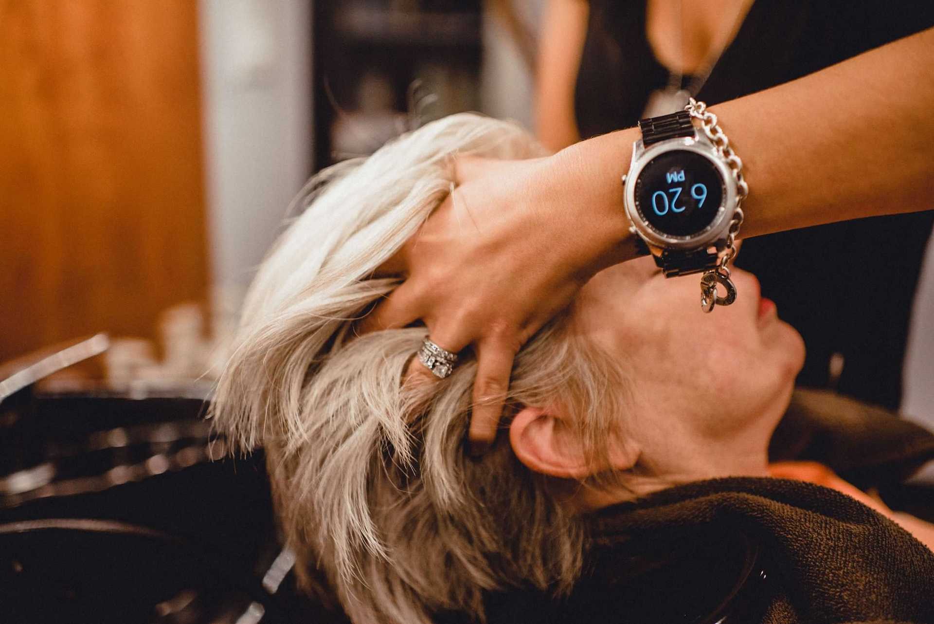 Person with short white hair getting a head massage while wearing a smart wristwatch showing 9:20.
