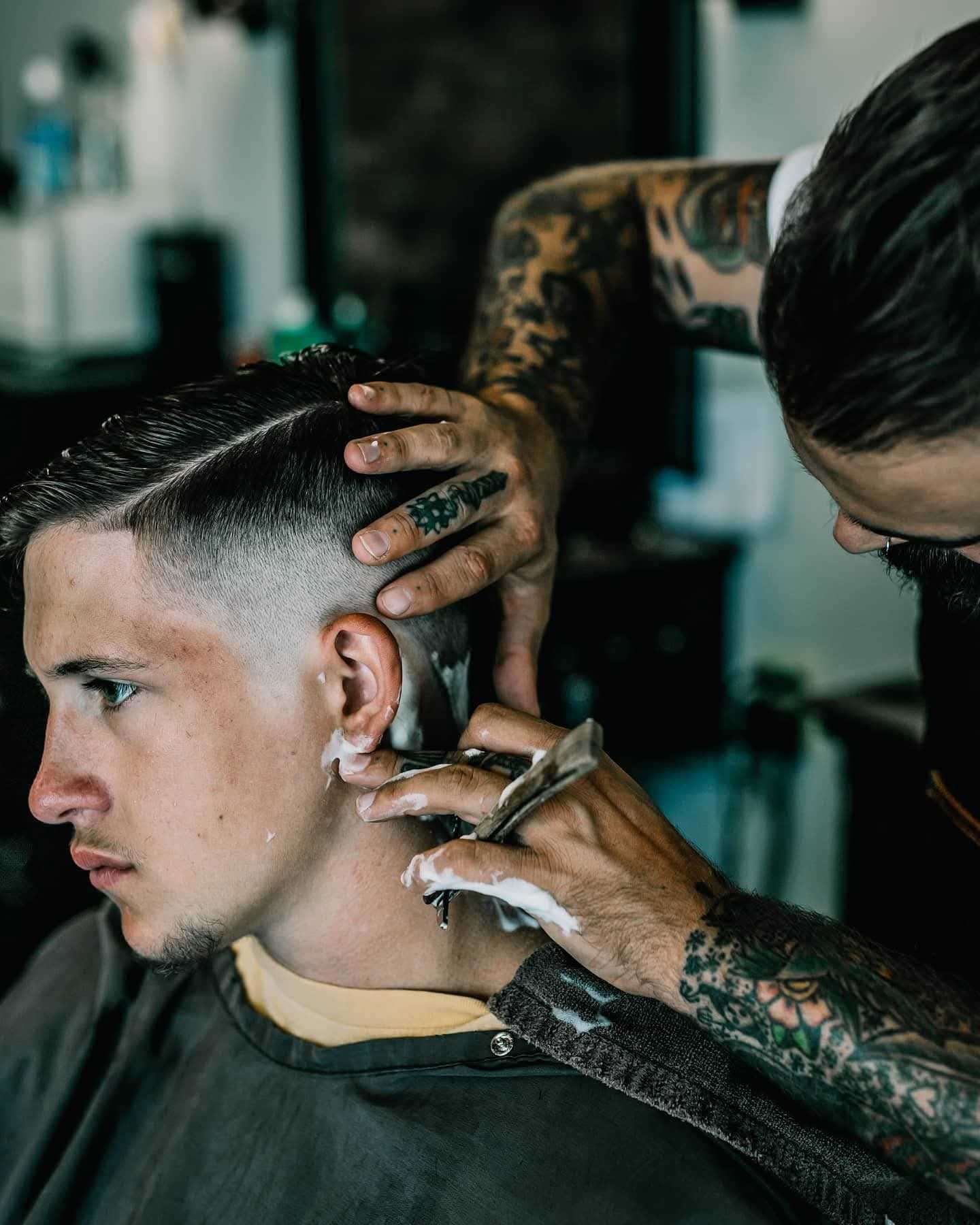Barber gives a young man a precise haircut using clippers and shaving cream.
