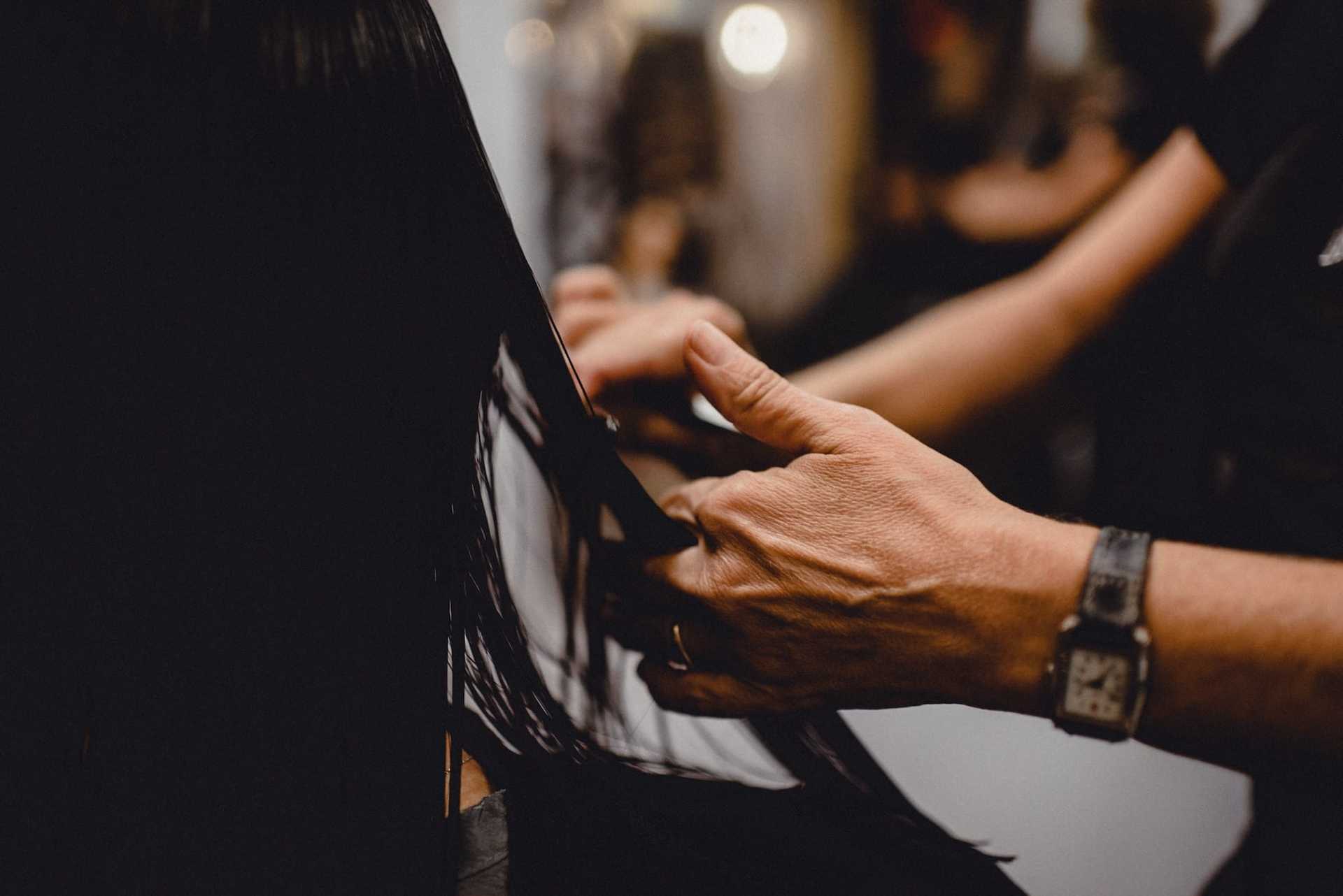 Close-up of a hairdresser's hands cutting long, wet black hair in a salon.
